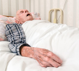 Elderly infirm man lying asleep in bed after being discharged from hospital.