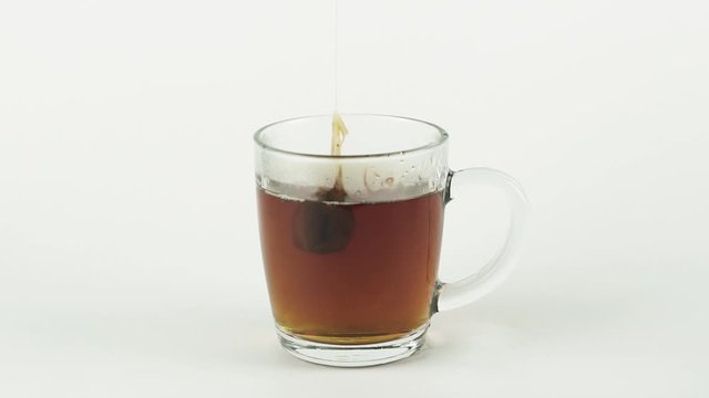 black tea bag lifting and dropping into glass transparent mug to brew tea isolated on white background slow motion close up