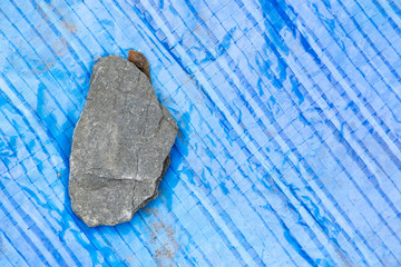 Fototapeta premium Vivid blue textured Tarpaulin cover with a random rock on top to keep the tarpaulin in place.