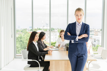 Portrait of Business woman leader self-confident standing in a busy modern workplace while Group of young business people working and communicating sitting at office desk together. union feminists