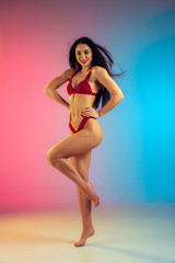 Fashion portrait of young fit and sportive caucasian woman in stylish red swimwear on gradient background. Brunette longhair model. Perfect body ready for summertime. Beauty, resort, sport concept.