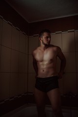 Fototapeta na wymiar Athletic good looking and attractive man with muscular body standing under running water in shower room