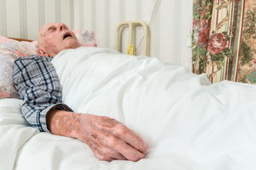 Elderly infirm man lying asleep in bed after being discharged from hospital.