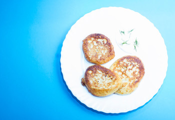 Dish of fried curd pancakes on a white plate on blue background