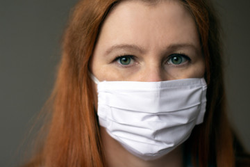 Portraite of a young red-haired woman wearing respiratory medical mask looking to the camera. Coronavirus 2019-ncov covid-19 concept.