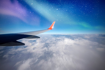 Fototapeta na wymiar Plane over north, Aurora or northern lights from airplane window, Aurora Borealis, night sky with clouds and stars