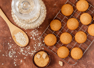 Fresh baked homemade wholegrain oatmeal flakes cookies on metal cooling rack. Useful, healthy dessert for gourmets. Ingredients on the table. Selective focus, top view