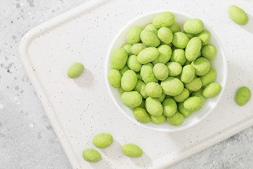 Fried peanuts in wasabi in a white bowl on a light gray table. Peanuts in wasabi close up