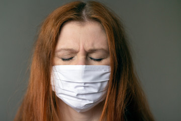 Portraite of a young red-haired woman wearing respiratory medical mask clothing her eyes. Coronavirus 2019-ncov covid-19 concept.