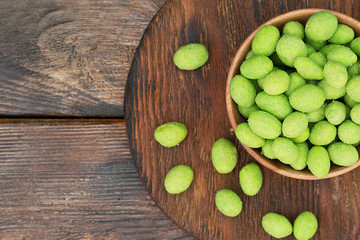 Fried peanuts in wasabi in a wooden bowl on a brown wooden table. Rustic style. Peanuts in wasabi...