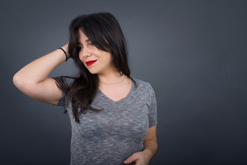 Shot of happy young woman with positive smile, has long hair, rejoices having weekend and good rest after hard working exhausting week, isolated on gray wall.
