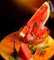 Fresh cocktail of watermelon juice glass and served with piece of watermelon and mint leaves over black slate background and wooden table. Healthy eating and drinking concept.