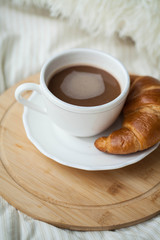 A cup of hot cocoa, a croissant, a wooden stand on the bed. Quarantine time. Homeliness.