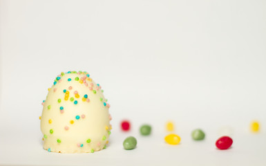 Fototapeta na wymiar Ei aus Schokolade mit bunten Zucker Streuseln isoliert vor weißem Hintergrund, Illustration von Ostern