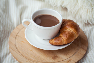 A cup of hot cocoa, a croissant, a wooden stand on the bed. Quarantine time. Homeliness.