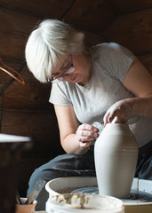 Female potter making a clay pot on a pottery wheel in her workshop