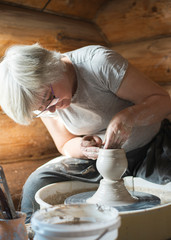Female potter making a clay pot on a pottery wheel in her workshop
