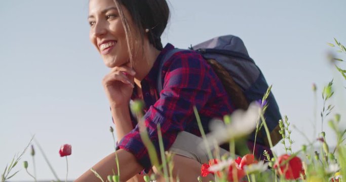 Smiling woman smelling and picking flowers from field.Side view,close-up,slow motion.Crouched smiling woman among red flowers outdoor. Sunny weather