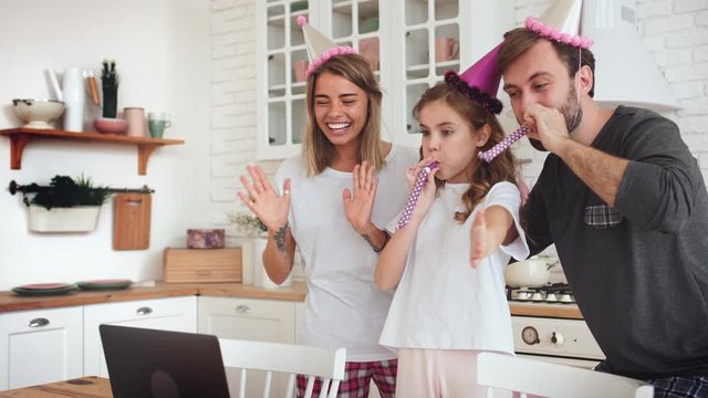 Happy family with a daughter celebrating birthday in kitchen using laptop for a video call during online birthday party and having some fun, slow motion
