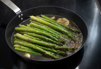 Cooking organic green asparagus in a pan on a black stove for a healthy vegetarian dinner