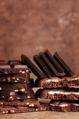 Composition of bars and pieces of different milk and dark porous chocolate with nuts and coconut on a brown background close-up side view