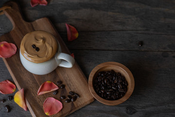 A cup of Dalgona coffee with coffee beans on a wooden table. Fluffy whipped drink.