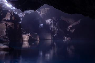 Underground lake in a hidden cave under a rocky mountain. The small rays of sunlight peaking in reflects the rock against the smoot water surface.