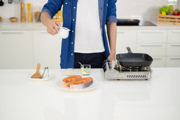 A man pour sauce on salmon steak in white kitchen.