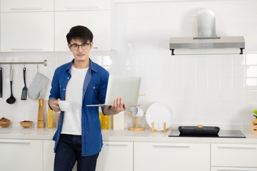 Asian freelance young man working from home with coffee using laptop in white kitchen