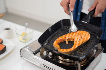 Asian man coking salmon steak with grill pan in white kitchen.Closed up salmon steak.