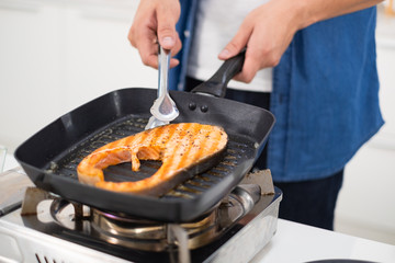 Asian man coking salmon steak with grill pan in white kitchen.Closed up salmon steak.