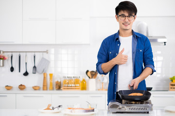 Asian man coking salmon steak with grill pan in white kitchen.