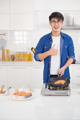 Asian man coking salmon steak with grill pan in white kitchen.