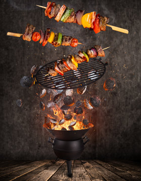 Kettle grill with hot briquettes, skewers and cost iron grate flying in the air. Freeze motion barbecue concept.