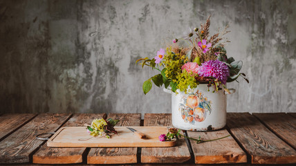 An ancient pot with a composition of flowers on a wooden rustic table against a concrete wall.