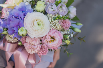 Flower arrangement in a pink hat box was created by a florist for a wedding gift. Flower bouquet of blue hydrangea, white Freesia, pink Ranunculus asiaticus, eustoma flowers, roses and eucalyptus