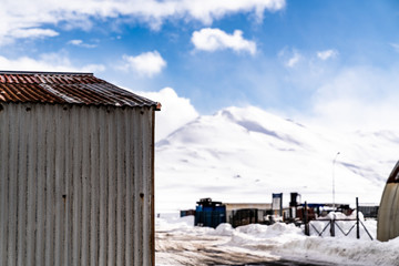 A grey rusty tool shed worn by weather in  the cold landscape of northern Iceland. A tall mountain covered in snow is seen behind it.