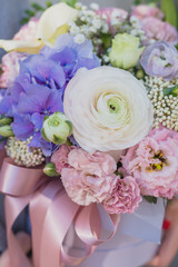 Flower arrangement in a pink hat box was created by a florist for a wedding gift. Flower bouquet of blue hydrangea, white Freesia, pink Ranunculus asiaticus, eustoma flowers, roses and eucalyptus