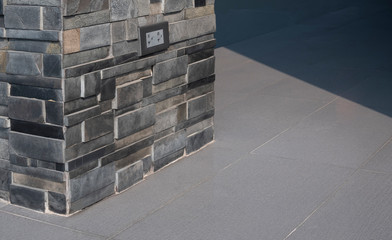 Electric outlet in slate stone pillar on grey tile floor outside of house building, architecture concept