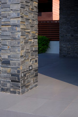 Close up slate stone pillar with sunlight and shadow on surface of gray tile floor outside of house building in vertical frame, exterior architecture concept