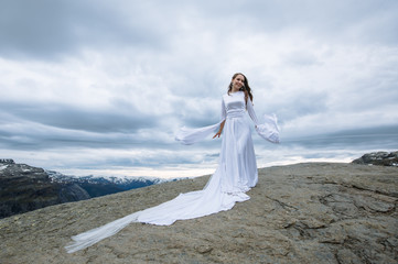 Fototapeta na wymiar a bride in a long wedding dress on a rock fragment in the mountains