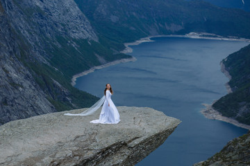 a bride in a long wedding dress on a fragment of Trolltunga rock in the mountains of Norway