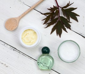 Ingredients for homemade facial mask. Coconut oil, shea butter, essential oil and bentonite clay on wooden spoon, white table. Good for face and neck.