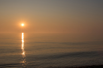 Fototapeta premium Beautiful misty morning sunrise over a calm sea. Soft sky and distant wind turbines.