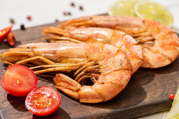 close up view of fried shrimps on wooden board with cherry tomatoes and lime