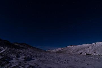 A starry dark blue sky in Iceland over the snow covered rocky landscape.