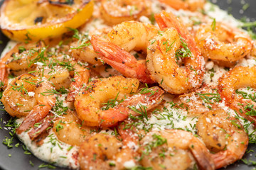 close up view of fried shrimps in sauce with dill and lemon in black plate