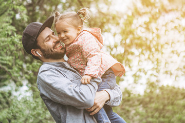 stylish bearded father with his little daughter in his arms against the backdrop of green trees on...