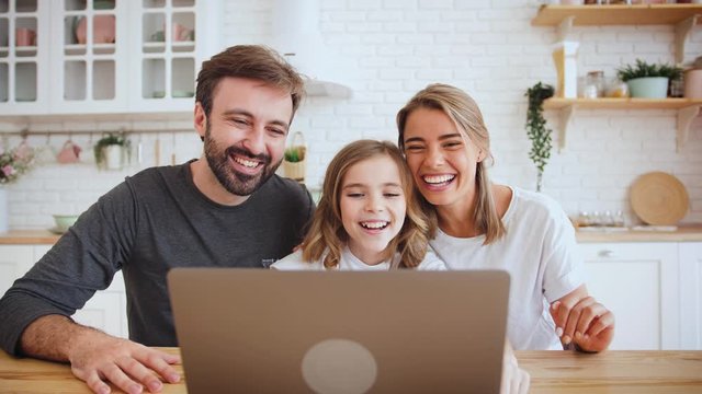 Portrait of happy positive family young using laptop computer for a video call in the kitchen and waving hands