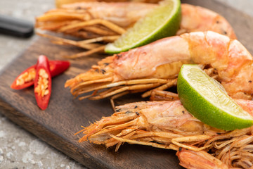 close up view of fried shrimps with chili and lime on wooden board